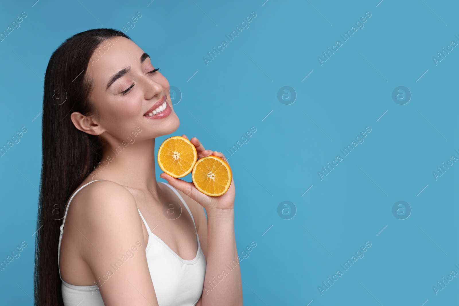 Photo of Beautiful young woman with pieces of orange on light blue background. Space for text