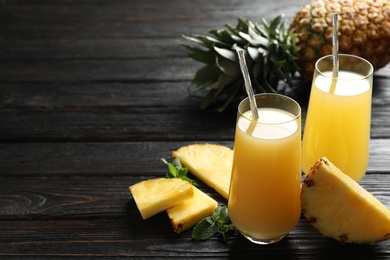 Photo of Delicious pineapple juice and fresh fruit on black wooden table. Space for text