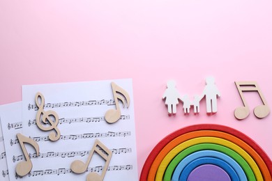 Baby songs. Music sheets, figures of family, wooden notes and toy rainbow on pink background, flat lay