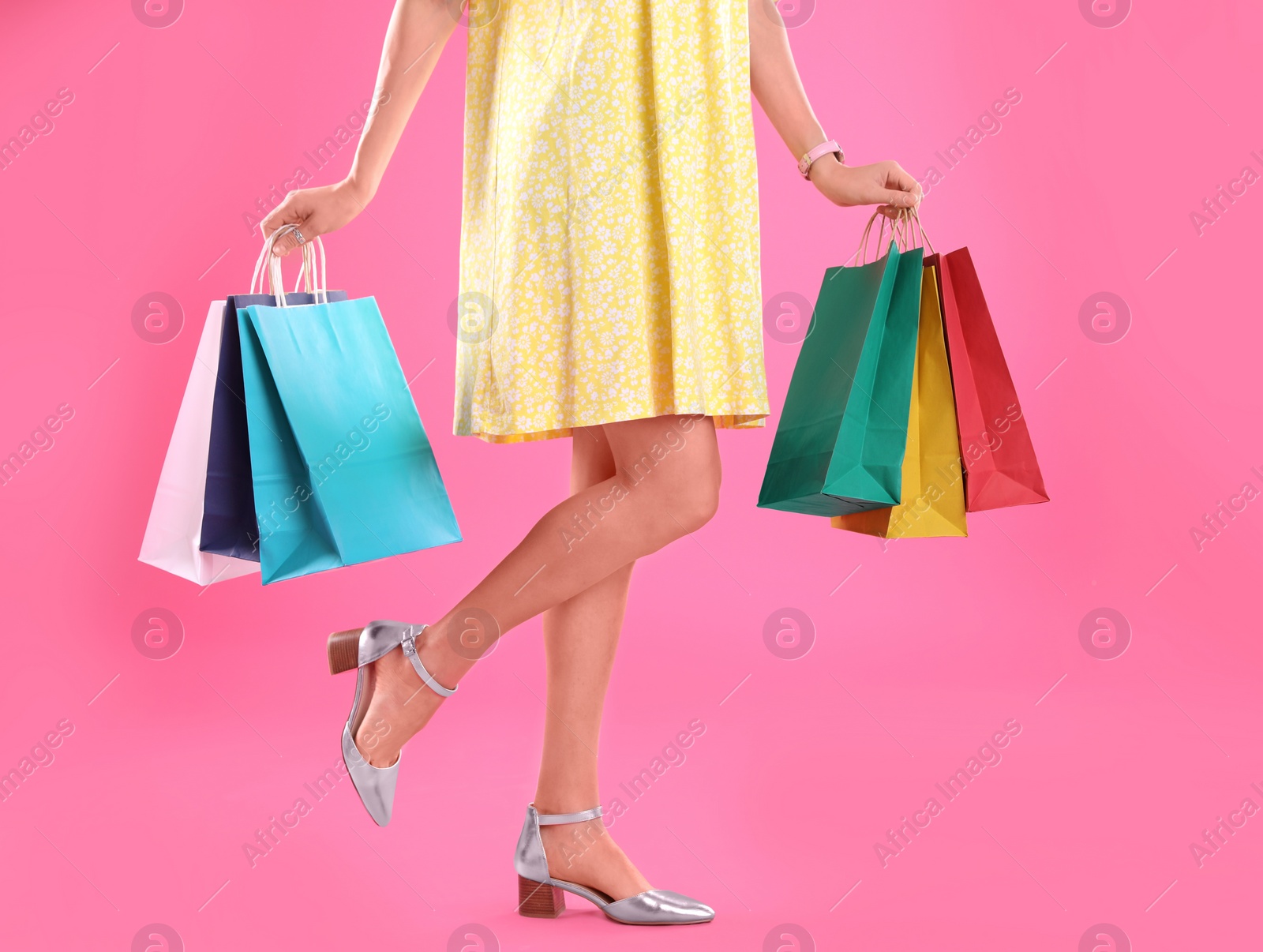 Photo of Young woman with shopping bags on color background, closeup of legs