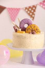 Delicious cake decorated with sweets and balloons on white wooden table