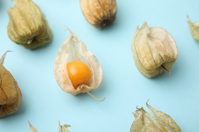 Photo of Ripe physalis fruits with calyxes on light blue background, closeup