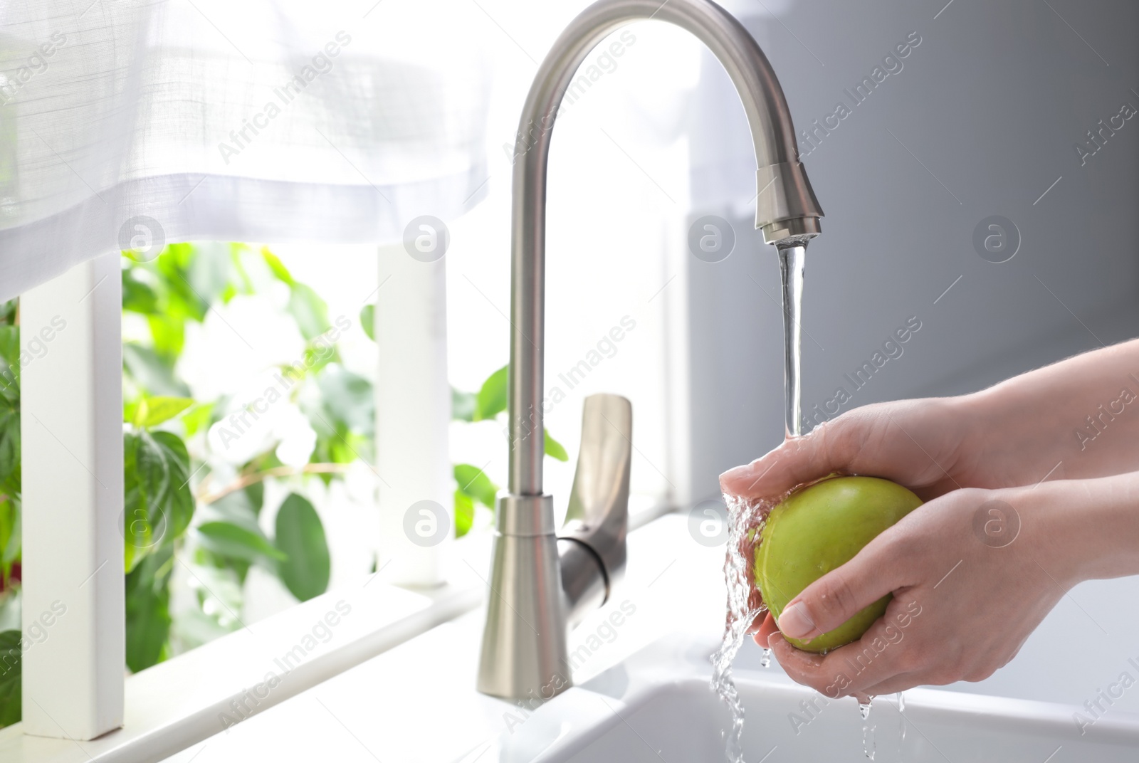 Photo of Woman washing apple over sink in kitchen, closeup. Space for text