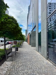 Photo of Sidewalk between modern buildings and trees along road in city