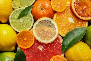 Sliced and whole citrus fruits with leaves as background, top view