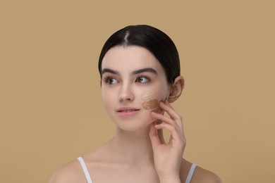 Photo of Teenage girl with swatches of foundation on face against beige background