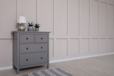 Photo of Grey chest of drawers near empty molding wall indoors, space for text