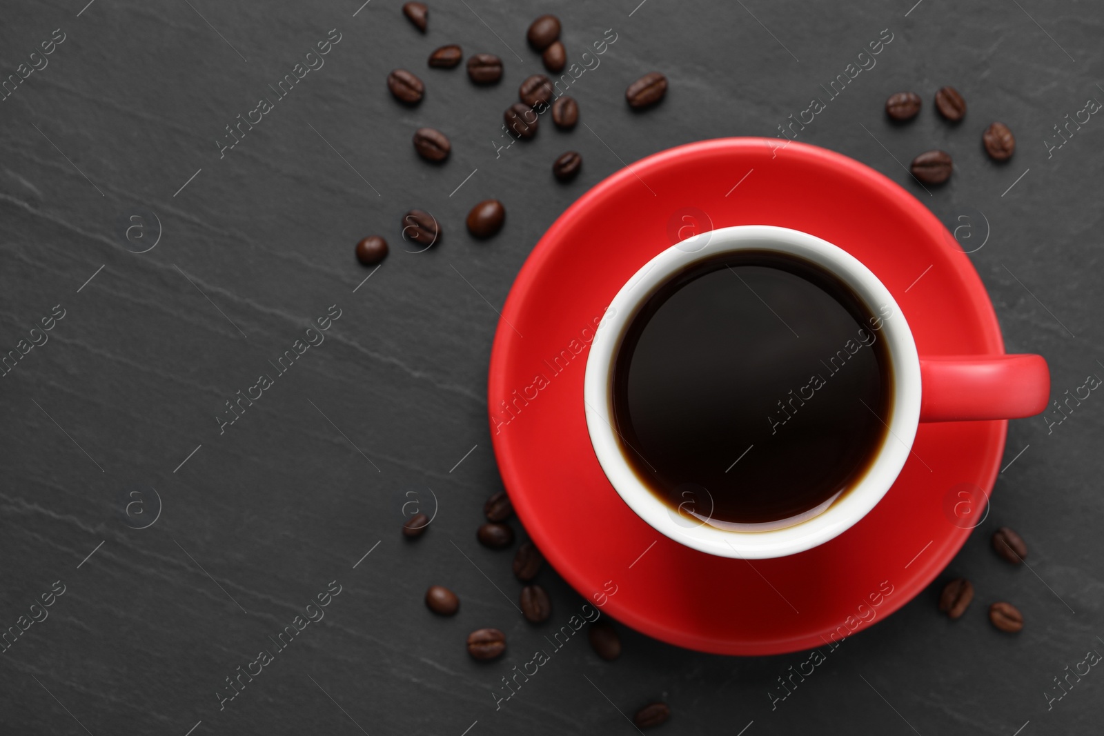 Photo of Cup with aromatic coffee and beans on black textured table, flat lay. Space for text