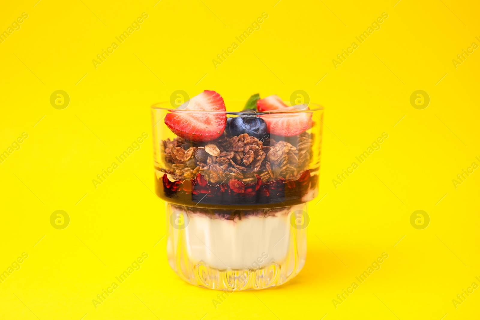 Photo of Tasty granola with berries, jam and yogurt in glass on yellow background