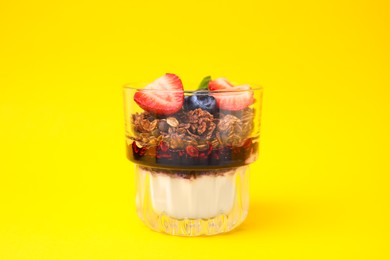 Photo of Tasty granola with berries, jam and yogurt in glass on yellow background