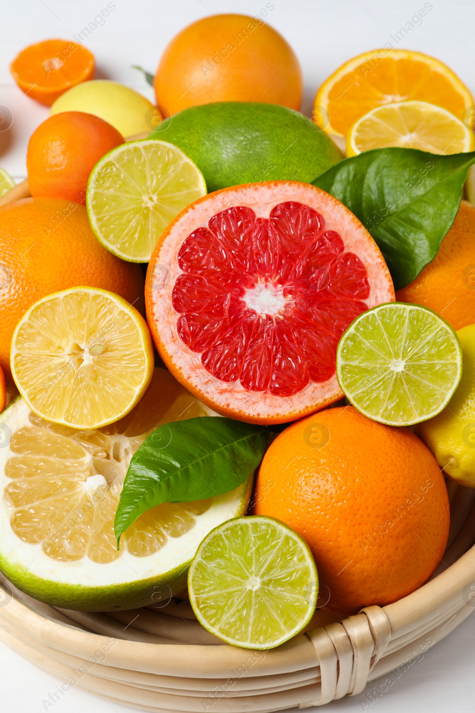 Photo of Different ripe citrus fruits with green leaves on white table