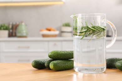 Refreshing cucumber water with rosemary in jug and vegetable on wooden table. Space for text