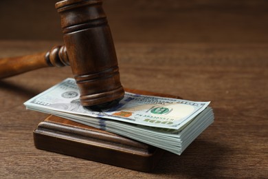 Photo of Law gavel with stack of dollars on wooden table, closeup