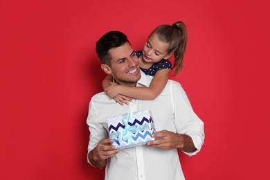 Man receiving gift for Father's Day from his daughter on red background