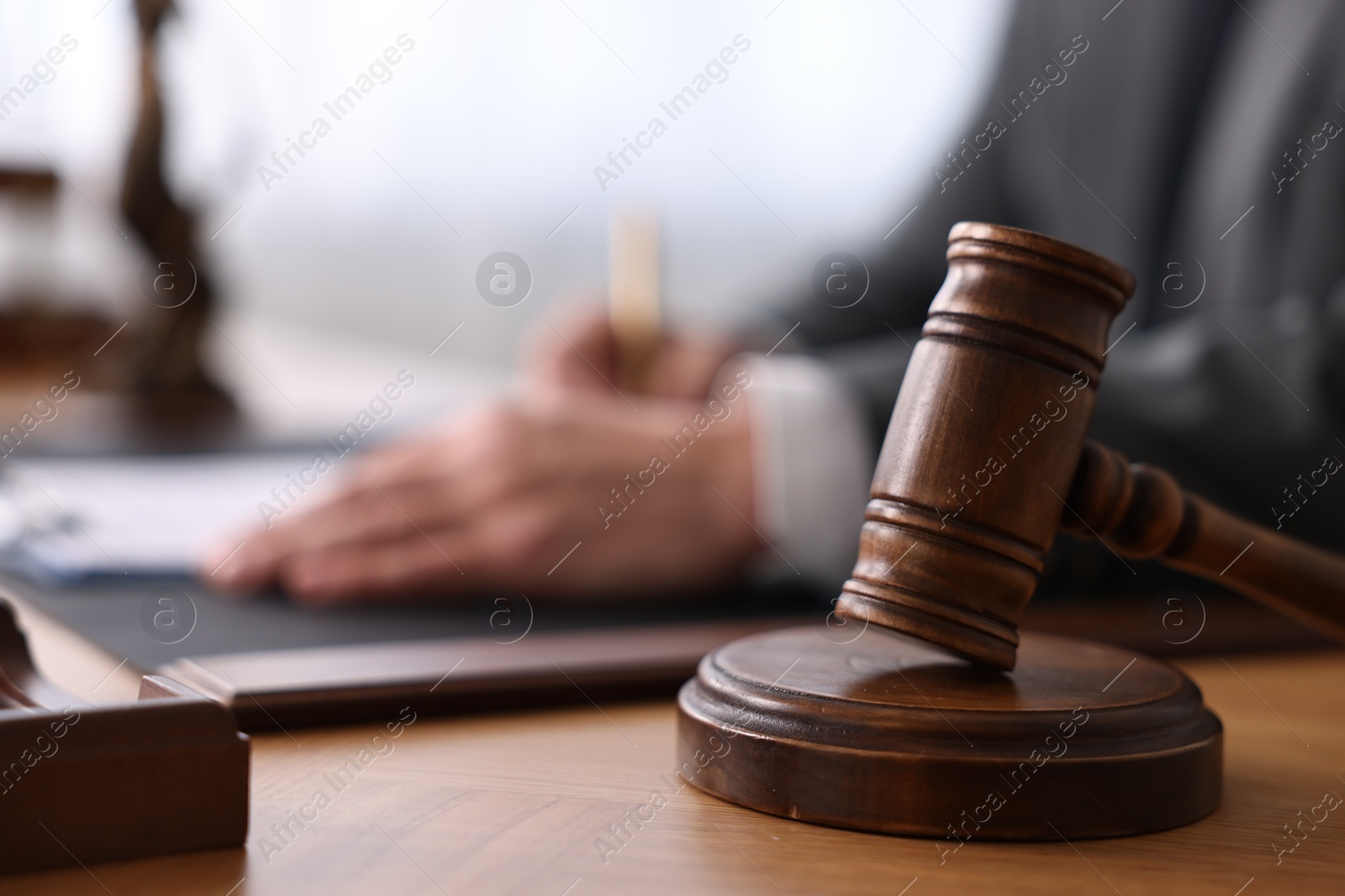 Photo of Notary writing notes at wooden table in office, focus on gavel