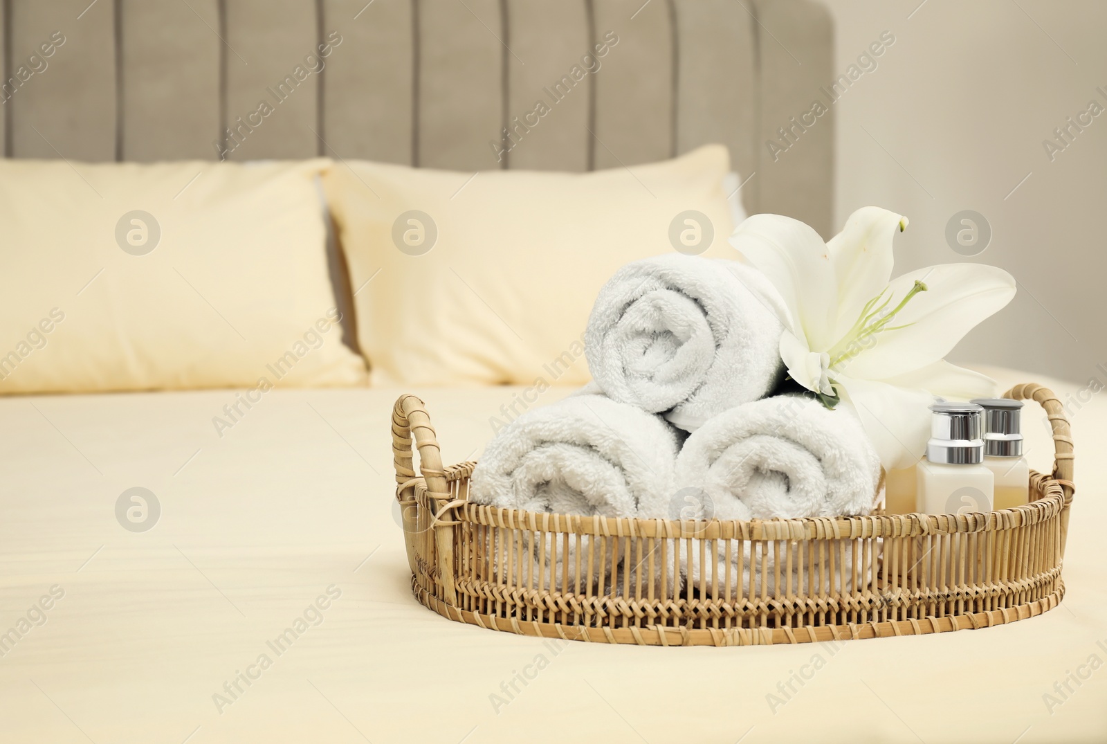 Photo of Rolled clean towels and shampoo bottles on bed. Space for text