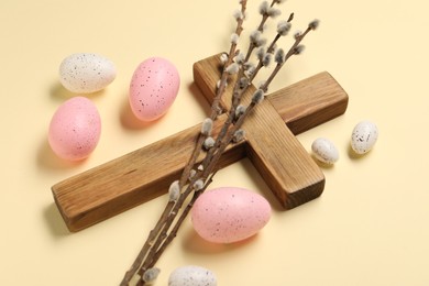 Photo of Wooden cross, painted Easter eggs and willow branches on beige background