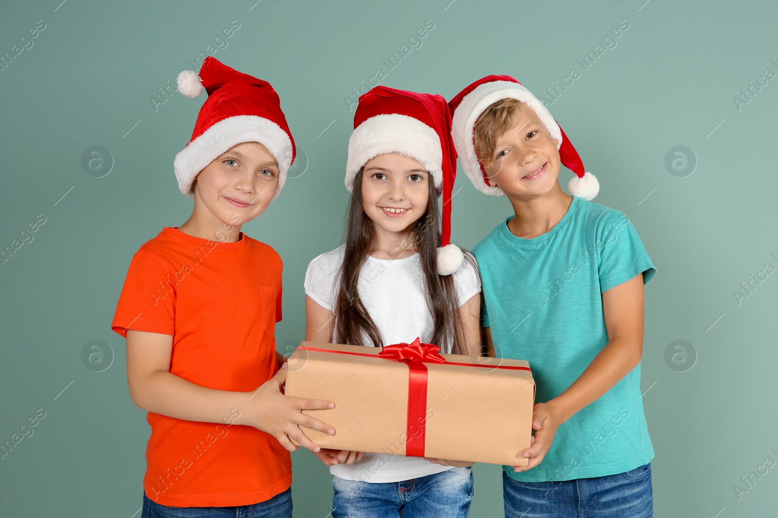 Photo of Cute little children in Santa hats with Christmas gift box on color background