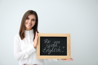 Young female teacher holding chalkboard with words DO YOU SPEAK ENGLISH? on light background