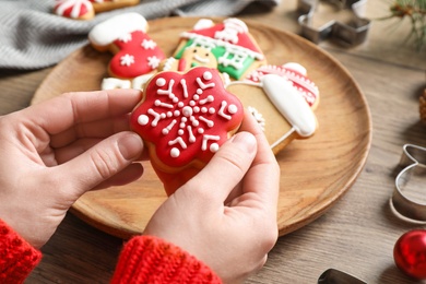Photo of Woman holding tasty homemade Christmas cookie over wooden table, closeup