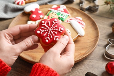 Woman holding tasty homemade Christmas cookie over wooden table, closeup