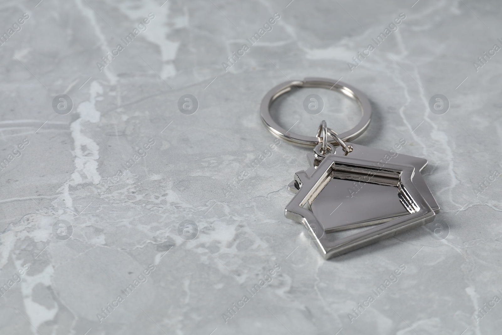 Photo of Metal keychain in shape of houses on grey marble table, closeup. Space for text