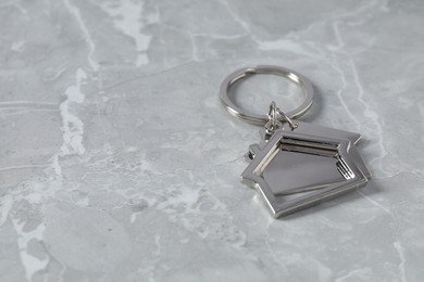 Metal keychain in shape of houses on grey marble table, closeup. Space for text