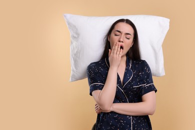 Photo of Tired young woman with pillow yawning on beige background, space for text. Insomnia problem