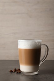 Glass cup of delicious layered coffee and beans on grey table against light background, space for text