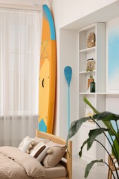 Photo of SUP board, bed and furniture in room. Interior design