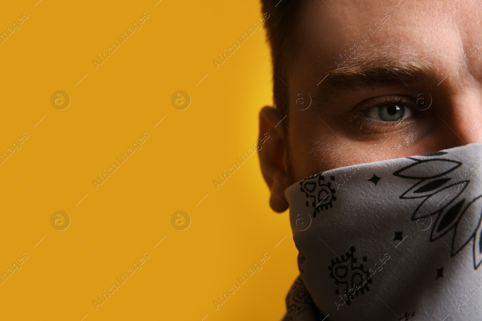 Photo of Young man with bandana covering his face on yellow background, closeup. Space for text