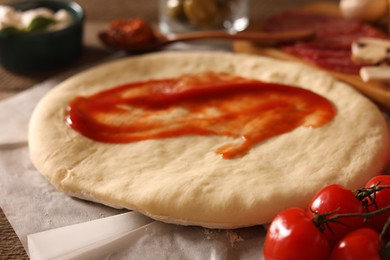 Photo of Pizza dough with tomato sauce and products on table, closeup