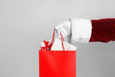 Santa holding paper bag with gift boxes on light grey background, closeup