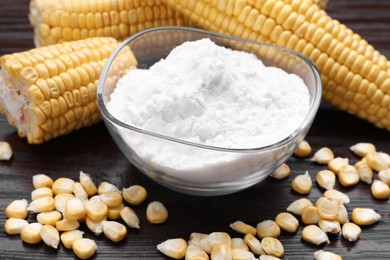 Photo of Bowl with corn starch, ripe cobs and kernels on dark wooden table, closeup