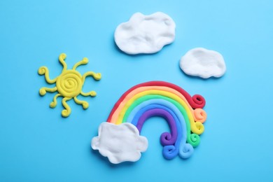 Photo of Rainbow, sun and clouds made from play dough on light blue background, flat lay