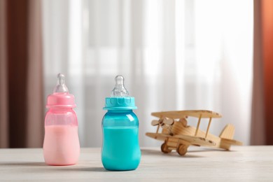 Photo of Feeding bottles with milk and toy plane on white wooden table indoors