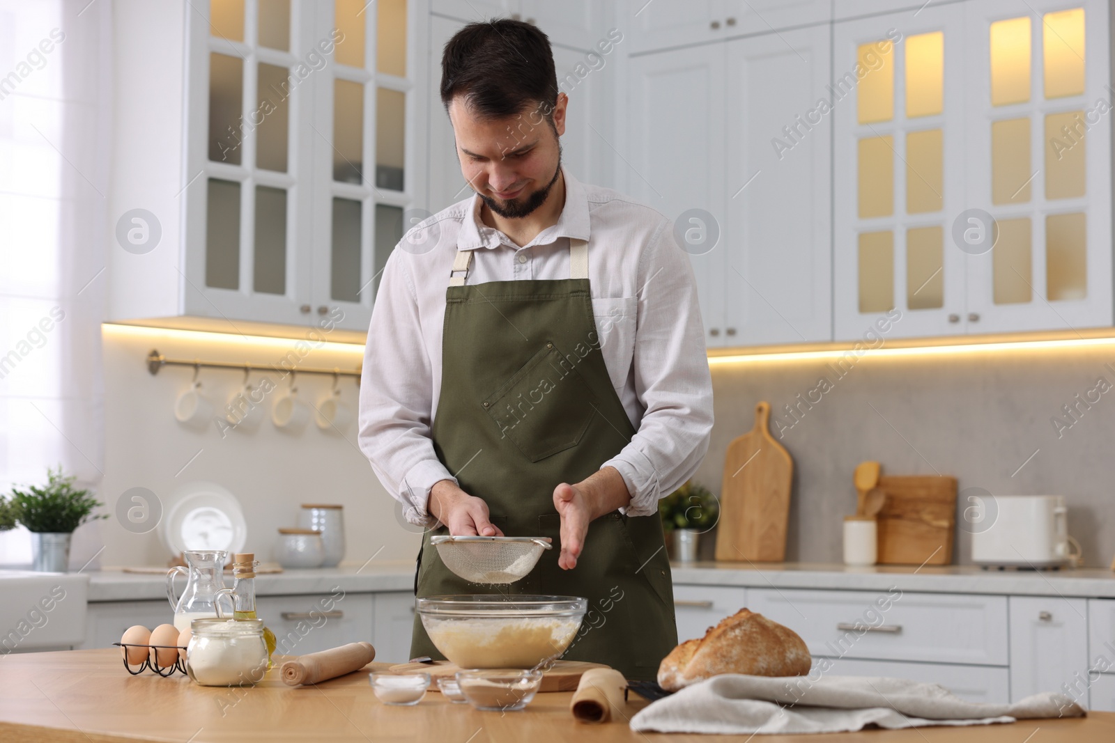 Photo of Making bread. Man sprinkling flour onto dough at wooden table in kitchen