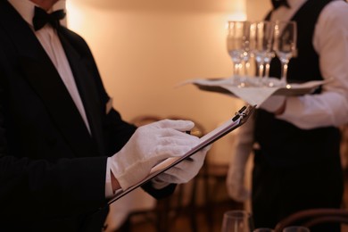 Photo of Man with clipboard teaching trainees indoors, closeup. Professional butler courses