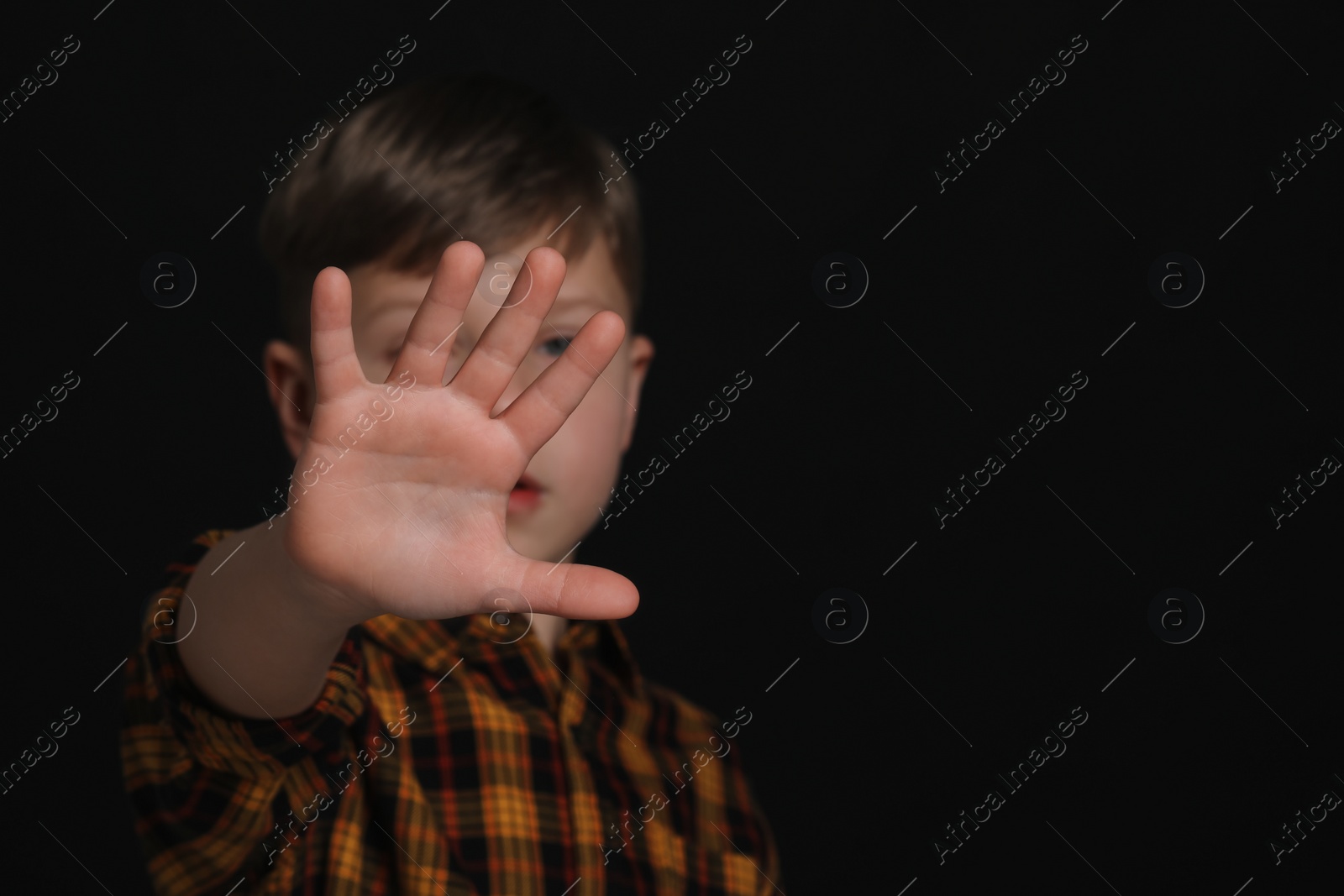 Photo of Boy making stop gesture against black background, focus on hand and space for text. Children's bullying