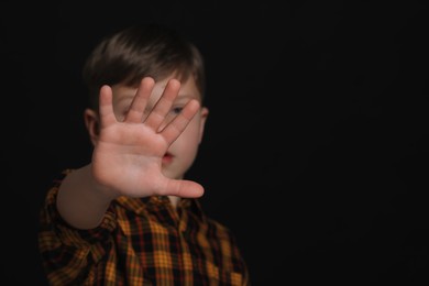 Boy making stop gesture against black background, focus on hand and space for text. Children's bullying