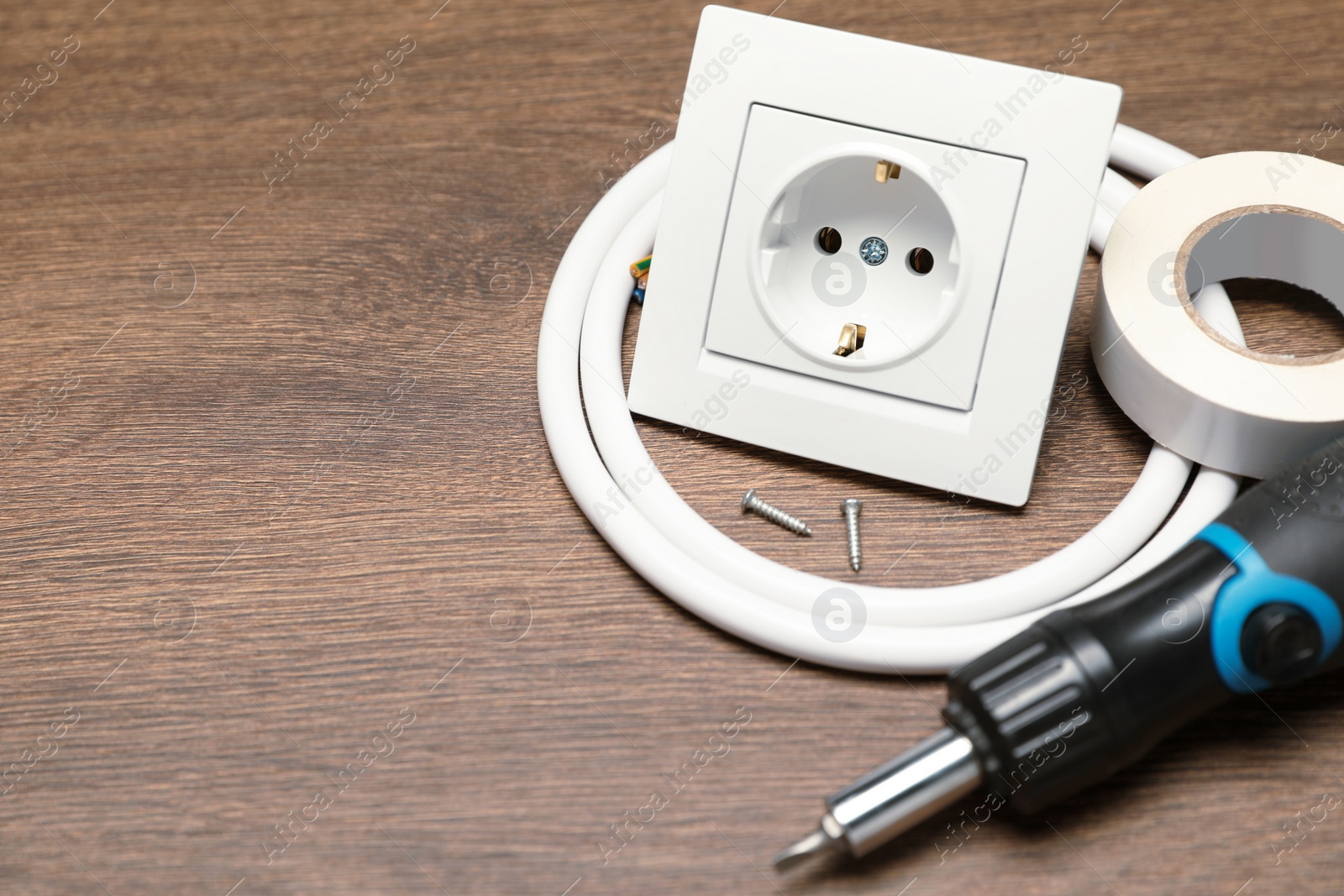 Photo of Power socket, screwdriver, cable and insulating tape on wooden table. Space for text