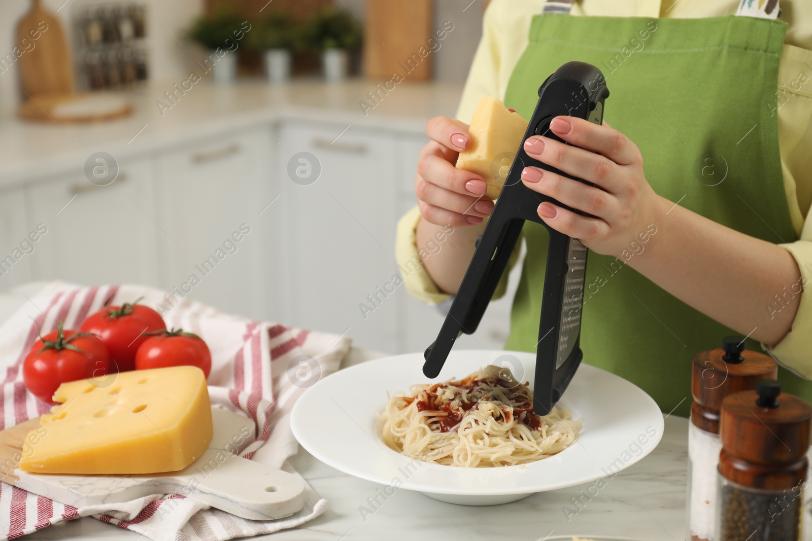 Photo of Woman grating cheese onto delicious pasta at white marble table in kitchen, closeup