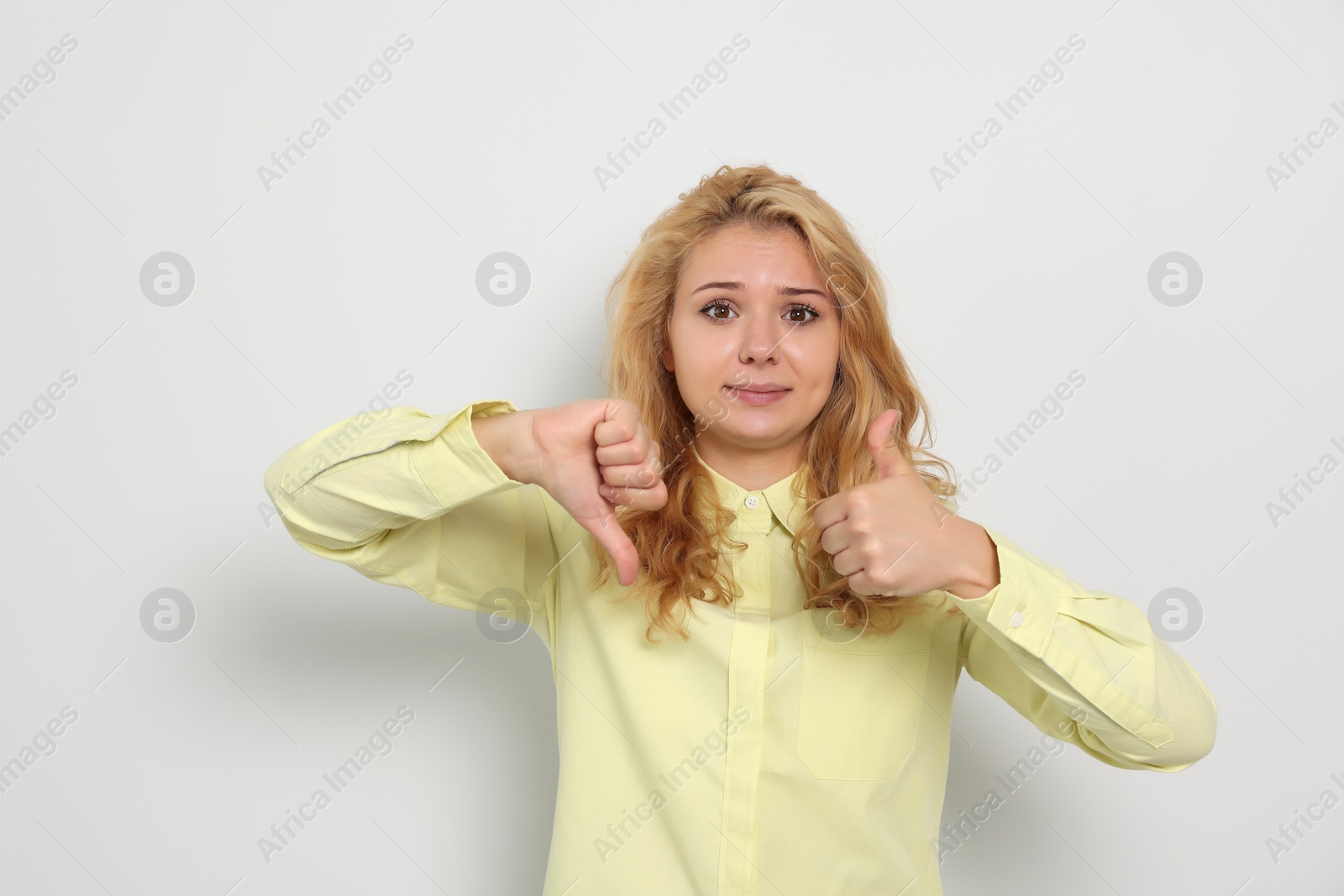 Photo of Conflicted young woman showing thumbs up and down gestures on white background