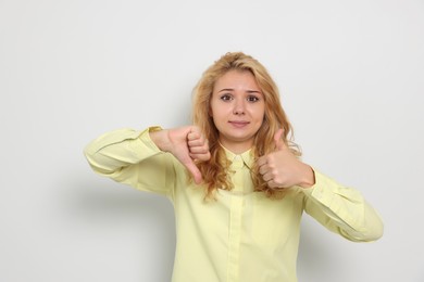 Photo of Conflicted young woman showing thumbs up and down gestures on white background
