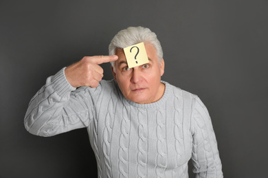 Emotional mature man with question mark on dark grey background