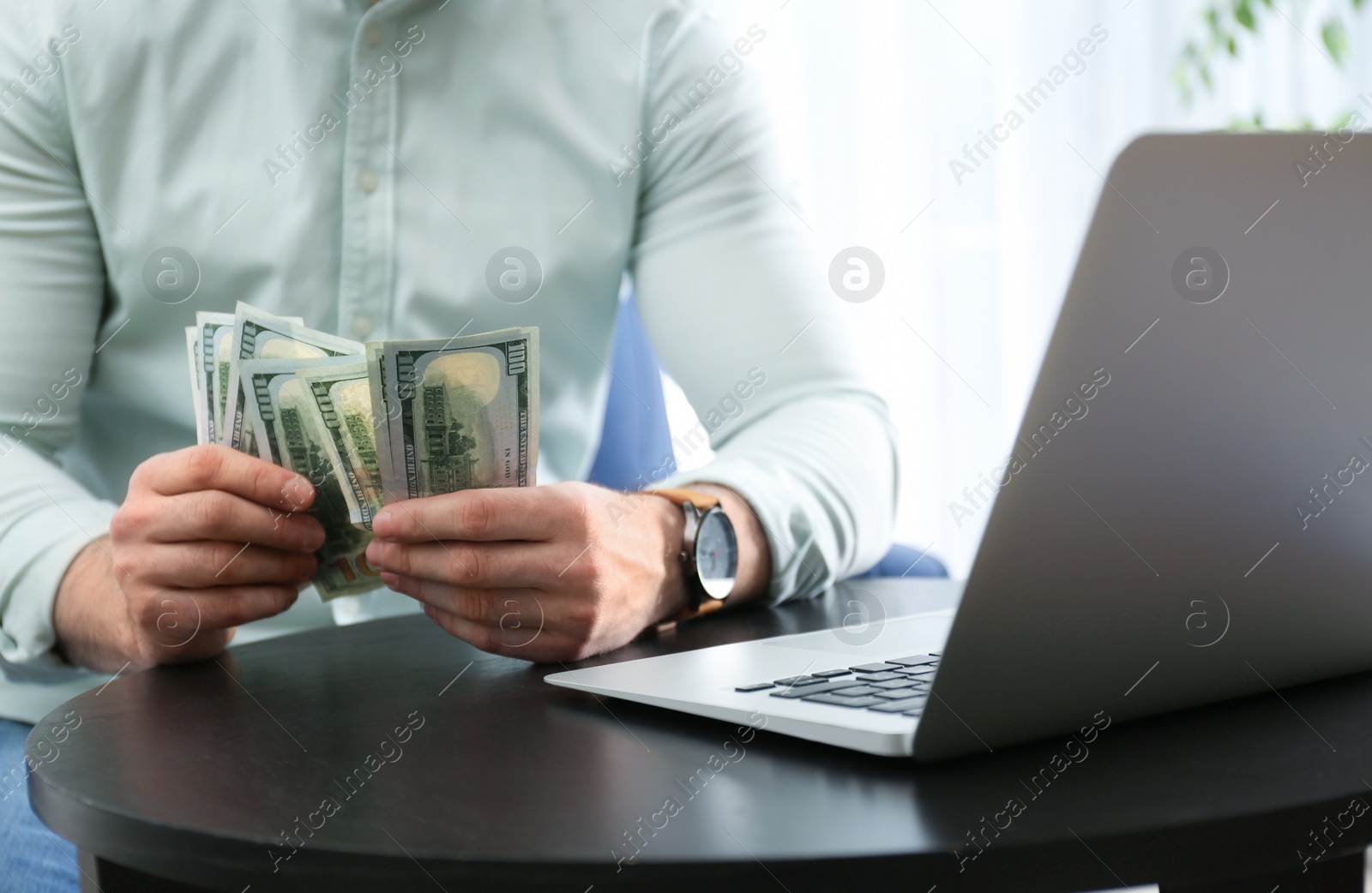 Photo of Businessman with laptop and money at table indoors, closeup