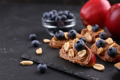 Photo of Fresh apples with peanut butter and blueberries on dark table, closeup. Space for text