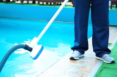 Photo of Male worker cleaning outdoor pool with underwater vacuum