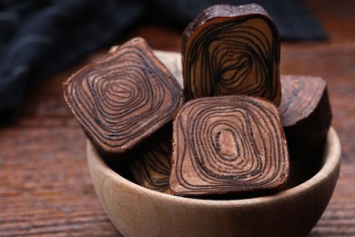 Bowl of tasty chocolate candies on wooden table, closeup