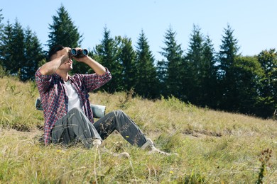 Tourist with hiking equipment looking through binoculars outdoors